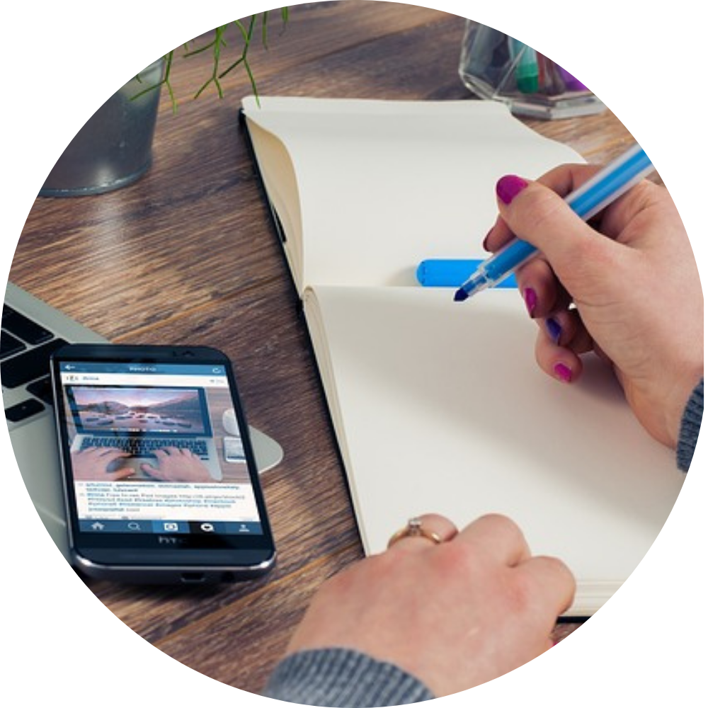 Hands taking notes in notebook next to phone